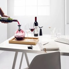 a person pours wine into a glass on a table next to a keyboard and computer