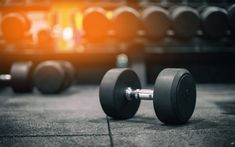 two dumbbells on the ground in front of rows of gym equipment