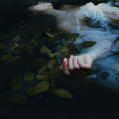 a woman floating in the water with her hands under her body and leaves around her