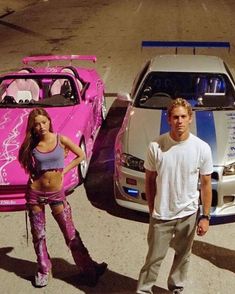 a man and woman standing next to two cars with pink paint on the hoods