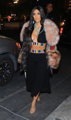 a woman in a crop top and skirt is walking down the street with her fur coat over her shoulders