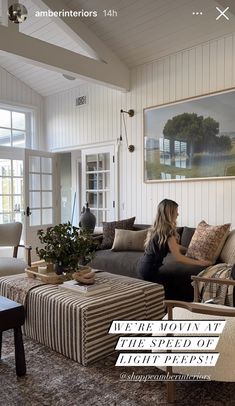 two women sitting on a couch in a living room with white walls and wood flooring