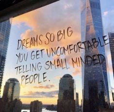 a window with writing on it in front of a cityscape that reads, dreams so big you get uncomfortableable telling small minds people