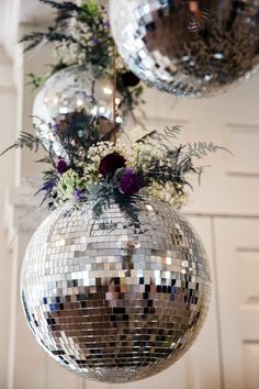 two disco balls hanging from the ceiling with flowers and greenery in them on display