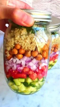 a person holding a mason jar filled with vegetables and chickpeas on the side