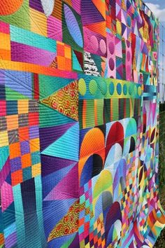 a large colorful quilt hanging on the side of a fence in front of a field