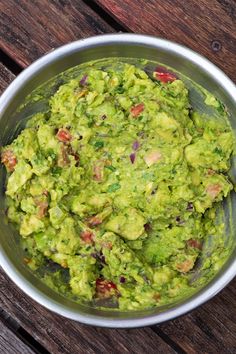 a metal bowl filled with guacamole on top of a wooden table