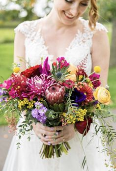 a bride holding a bouquet of flowers in her hands and smiling at the camera while standing outside