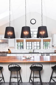 a kitchen with white cabinets and black pendant lights over the island, along with four bar stools