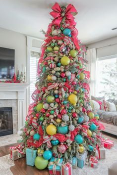 a christmas tree decorated with colorful ornaments and bows is in the middle of a living room