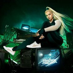 a woman sitting on top of a tv next to a green wall with neon lights