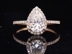 an engagement ring with a pear shaped diamond surrounded by smaller round diamonds on a black background