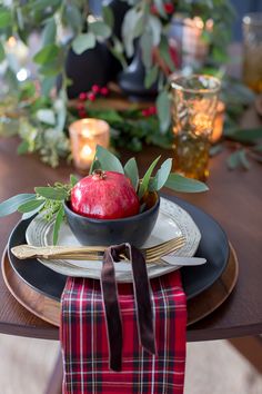 an apple sits in a bowl on top of a place setting with greenery and candles