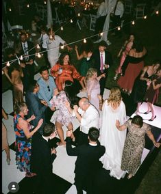 a group of people standing around each other on a dance floor with string lights strung over them