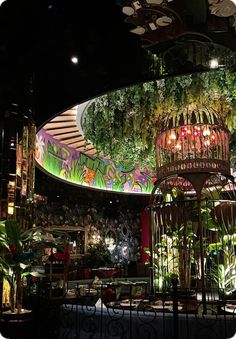 a birdcage filled with lots of greenery next to a ceiling covered in lights