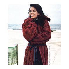 a woman standing on the beach wearing a red coat