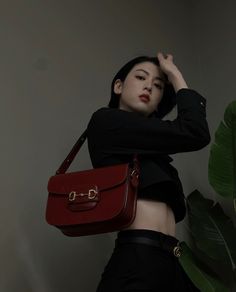 a woman holding a red purse standing next to a plant