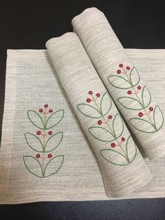 two white napkins with red berries on them sitting on a black table top next to each other