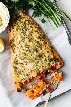 baked salmon fillet with herbs and lemons on a baking sheet next to a bowl of mayonnaise