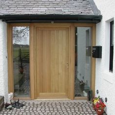 a wooden door sitting next to a white building with potted plants on the ground