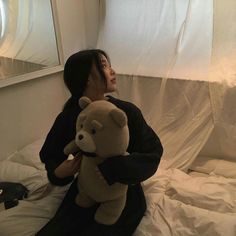 a woman sitting on a bed holding a teddy bear