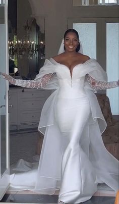 a woman in a white wedding gown and long sleeved dress with her arms out