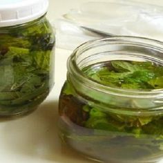 two jars filled with green leaves sitting on top of a white counter next to each other