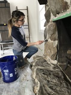 a woman is painting a stone fireplace in her home