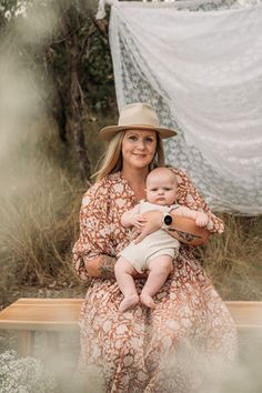 a woman sitting on a bench holding a baby in her arms and looking at the camera