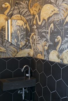 a bathroom with black tile and yellow flamingos on the wall, along with a sink