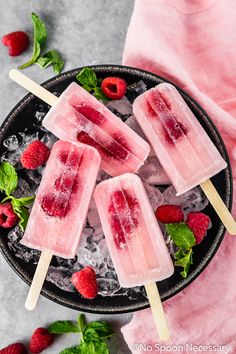 three popsicles with ice and raspberries on a black plate next to mint leaves