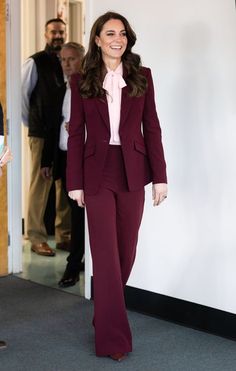 a woman in a red suit and pink shirt is walking down the street with other people behind her