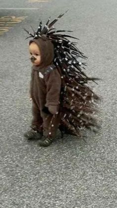 a baby dressed up in a costume with spikes on it's head is walking down the street