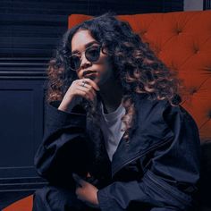 a woman sitting in a red chair with her hand on her chin and looking off to the side