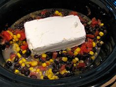 a crock pot filled with black beans and corn next to a block of butter