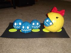 an orange and blue plastic toy sitting on top of a black mat next to three eggs