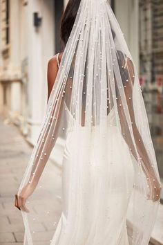 a woman is walking down the street wearing a wedding dress and veil with pearls on it