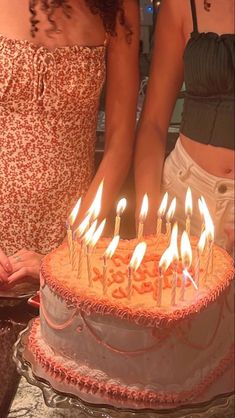 two women standing in front of a cake with lit candles