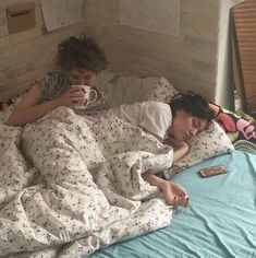 two people laying in bed and drinking coffee