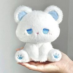 a hand holding a white stuffed animal with blue eyes