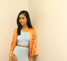 a woman standing next to a white wall wearing a skirt and orange blazer jacket