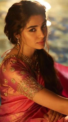 a woman in a pink sari sitting next to a pool with her hand on her hip