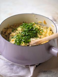 a pot filled with pasta and parsley on top of a white cloth next to a wooden spoon