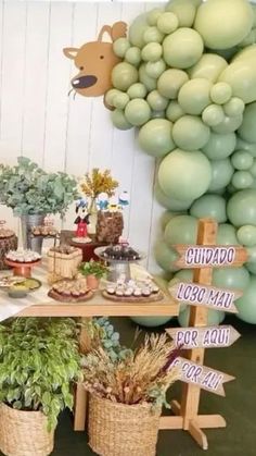 a table topped with lots of food next to balloons and greenery on the wall