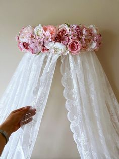 a person is placing flowers on the top of a canopy over a bed with sheer curtains