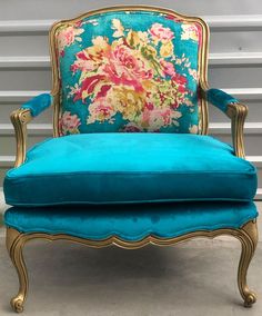 a blue velvet chair with gold trimming and flowers on the back, sitting in front of a striped wall