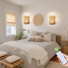 a person holding a remote control in front of a bed with white sheets and pillows