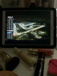 an ipad with makeup on top of it next to lipstick and other cosmetics items in front of the screen