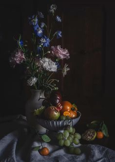 a vase filled with lots of different types of flowers next to fruit on a table