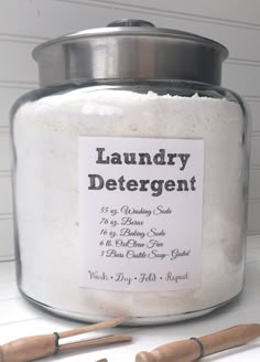 a large jar filled with laundry detergent next to two wooden utensils